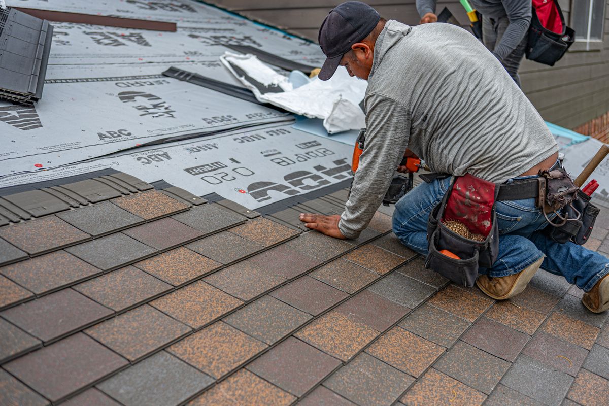 A roofer fitting new asphalt shingles alongside underlayment